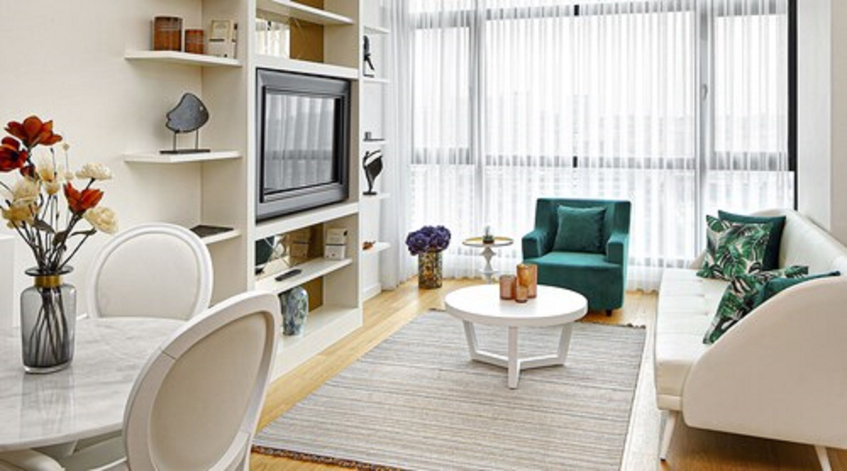 Un soggiorno con un divano bianco, una poltrona verde acqua, un tavolino da caffè e una TV su un mobile bianco.