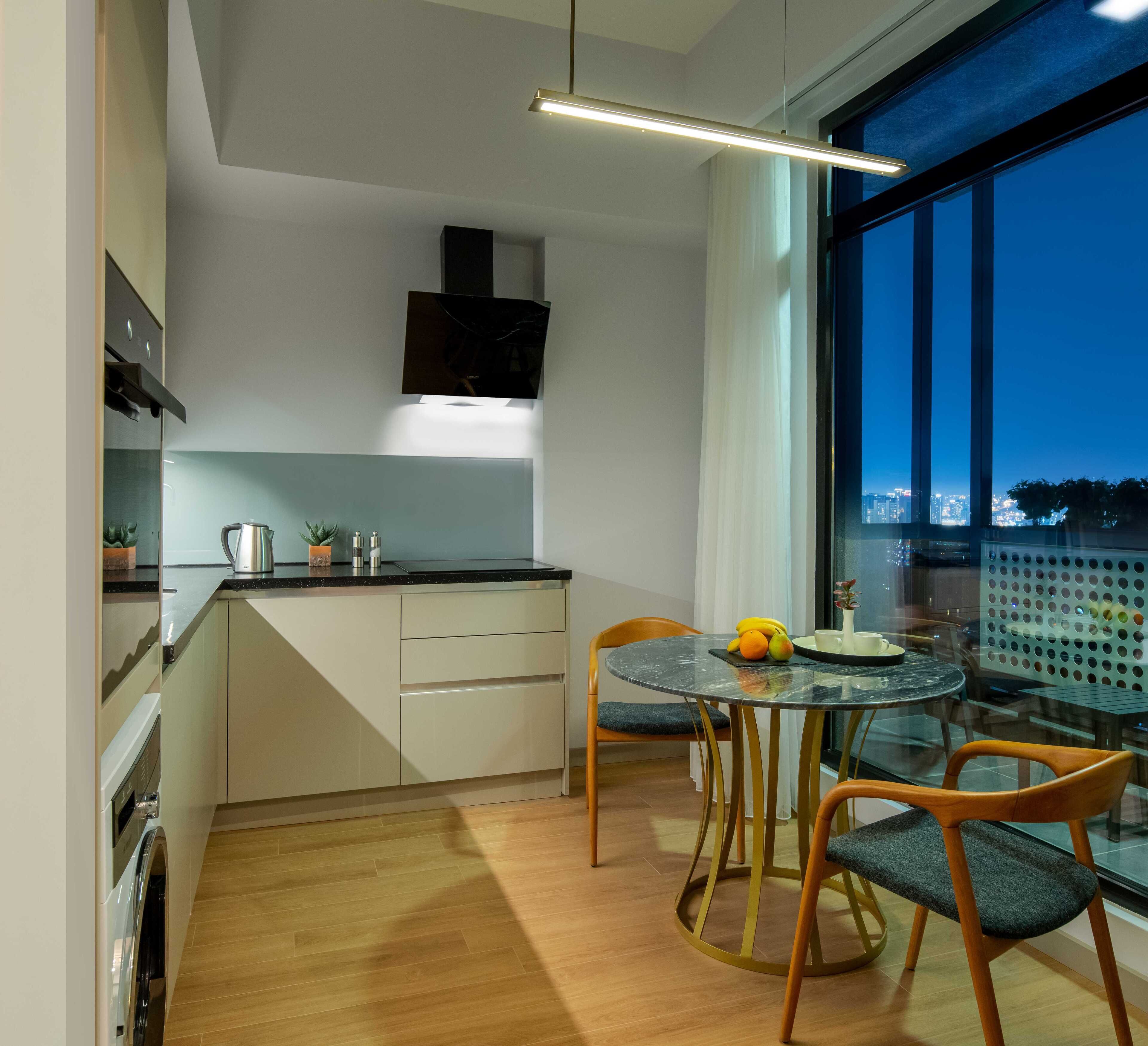 A modern kitchen with a dining area, wooden flooring, and a large window with a city view.