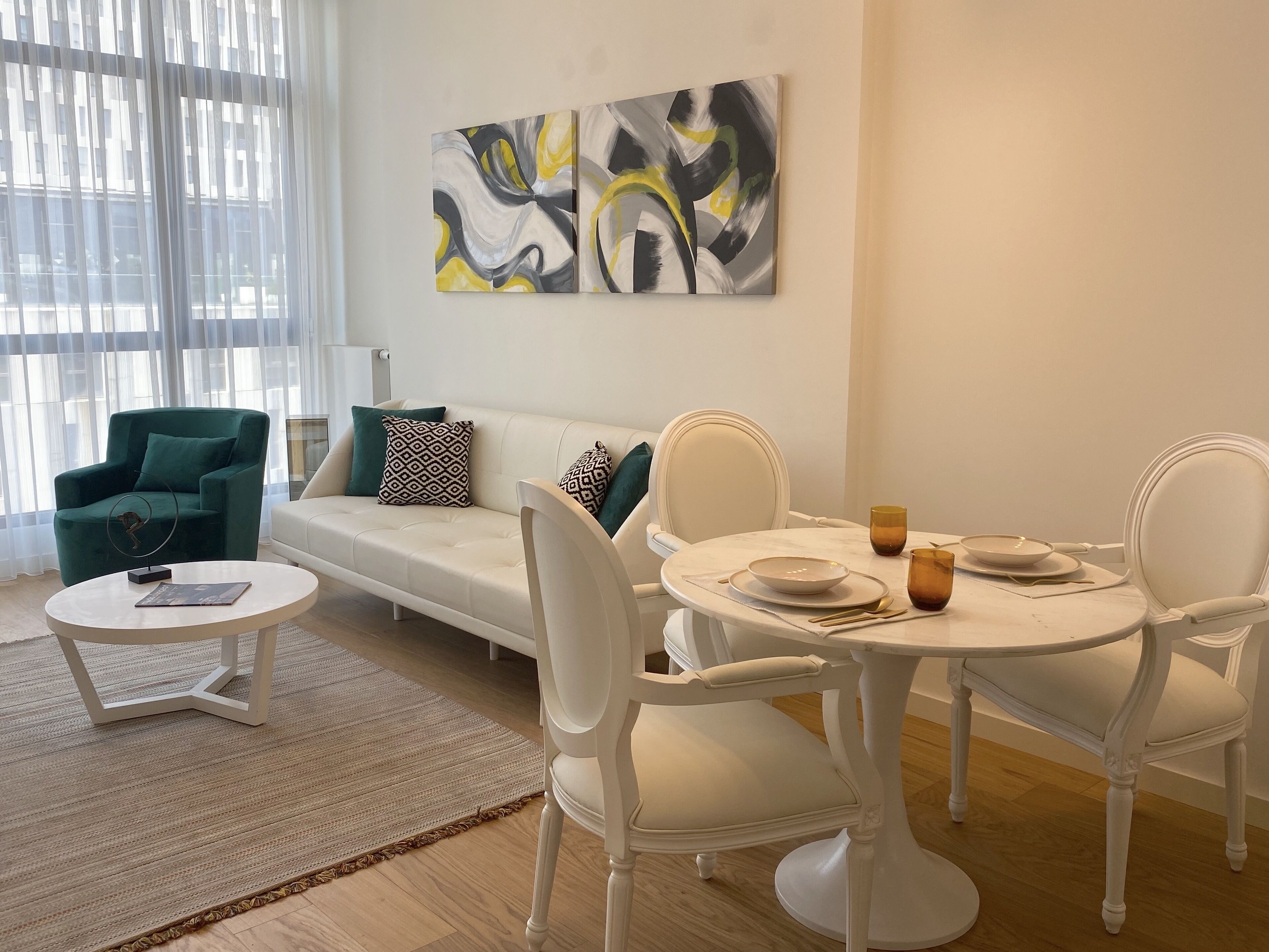 Uma sala de estar moderna com um sofá branco, poltrona verde e uma mesa de jantar posta com pratos e copos.