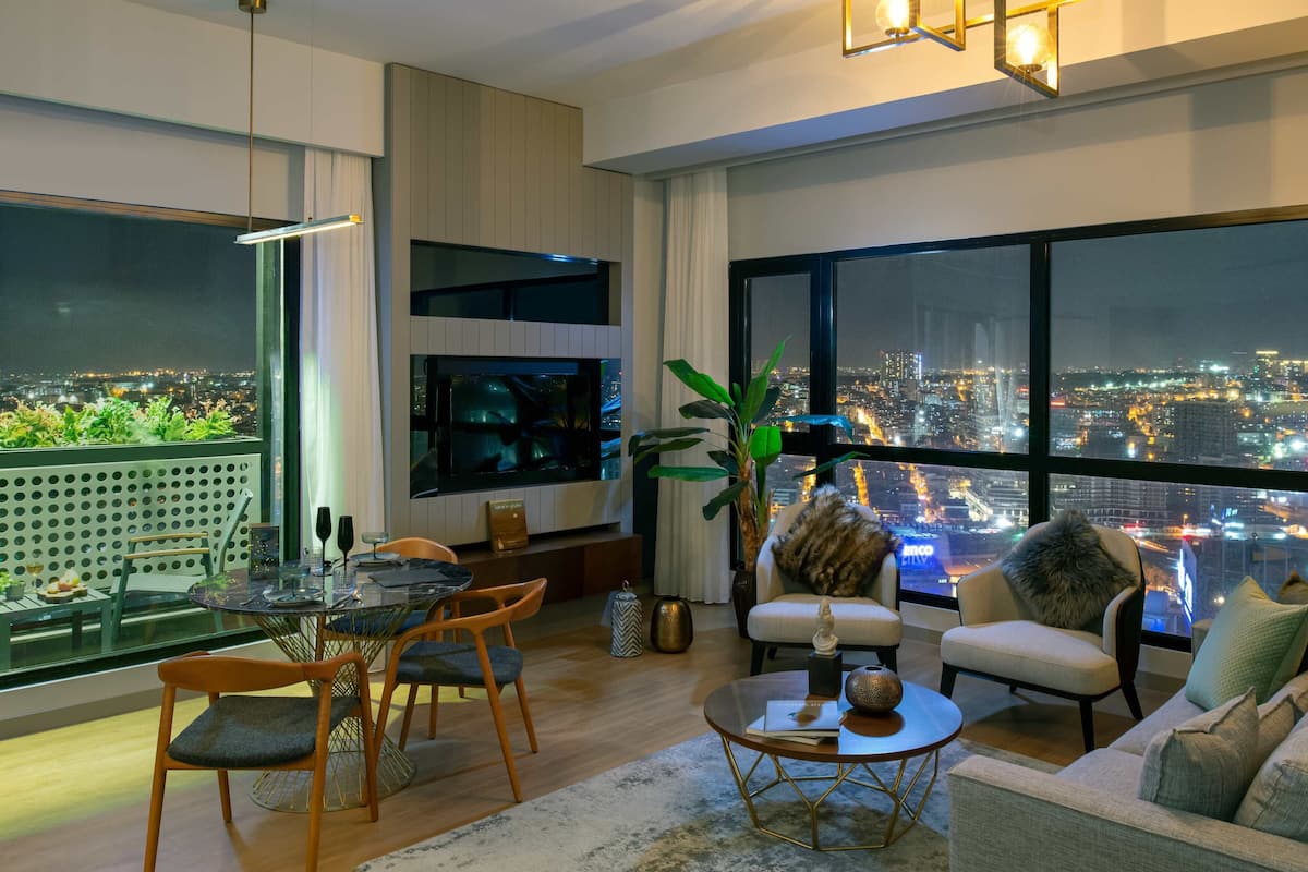 A modern living room with a city view, a dining area with a glass table, and a cozy seating area with a sofa and chairs.