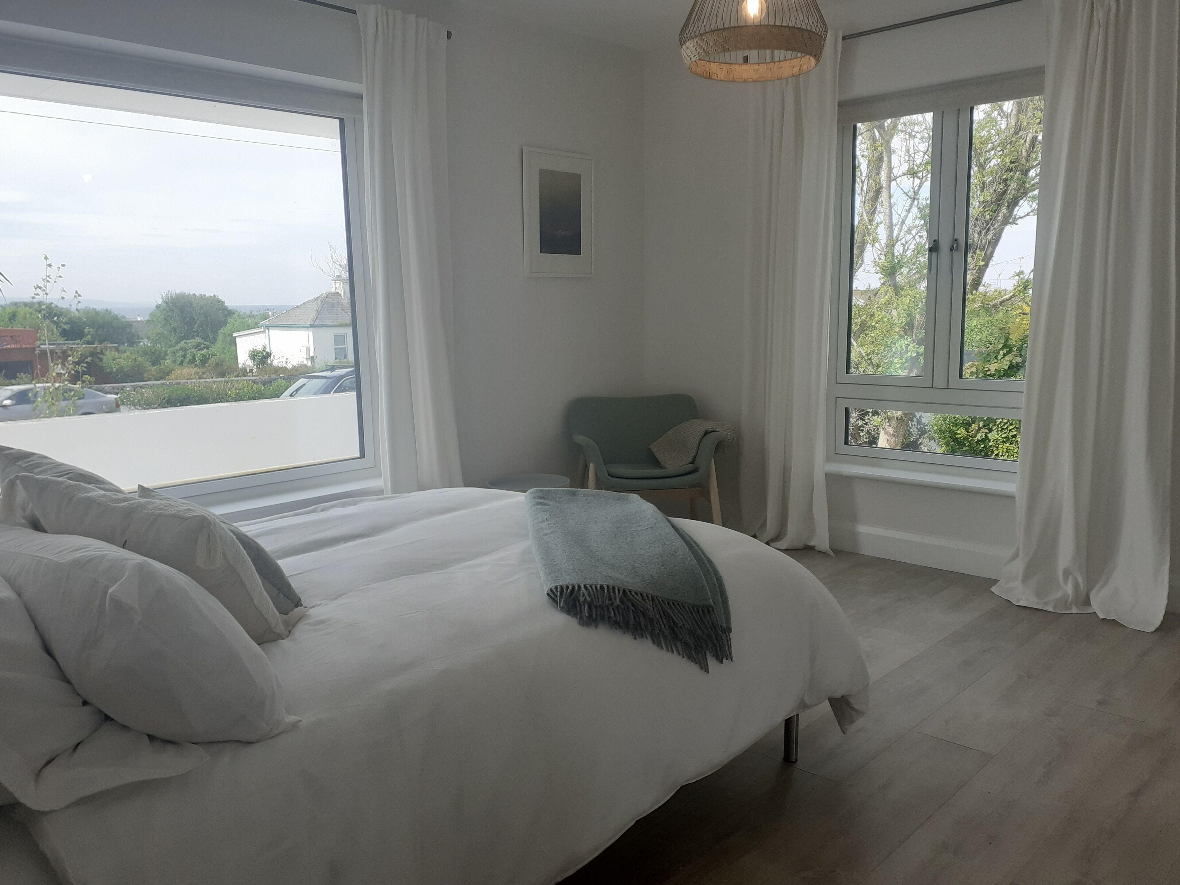A bedroom with a large bed, two windows, a chair, and a hanging light fixture.