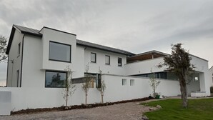 Moderni, kaksikerroksinen talo, jossa on valkoinen julkisivu, suuret ikkunat ja sorapäällysteinen ajotie.