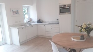 Moderni keittiö, jossa on valkoiset kaapit, sisäänrakennettu uuni sekä ruokailutila, jossa on pyöreä pöytä ja tuolit.