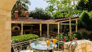 An outdoor patio with a round glass table, white cushioned chairs, and a stone wall. - Villa Anna Maria 3 Bedroom Private Pool (Heraklion)