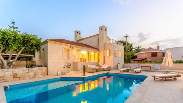 A poolside area with a stone pool, outdoor furniture, and a building with a stone facade and tiled roof. - Villa Anna Maria 3 Bedroom Private Pool (Heraklion)