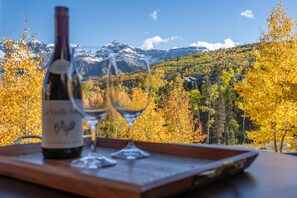 Une bouteille de vin et deux verres sur un plateau en bois, avec une vue sur les montagnes en arrière-plan.