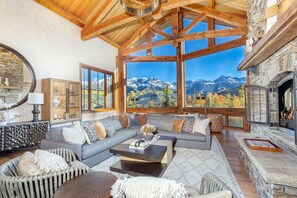 A spacious living room with a large window offering a mountain view, a stone fireplace, and a cozy seating area. - PICTURE PERFECT- Stunning Ski-In/Out Trailside Manor Perfect for Groups (Mountain Village)