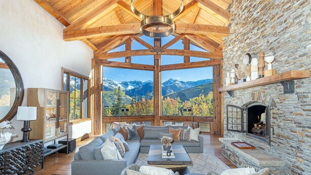 A spacious living room with a large window offering a mountain view, a stone fireplace, and a cozy seating area. - PICTURE PERFECT- Stunning Ski-In/Out Trailside Manor Perfect for Groups (Mountain Village)