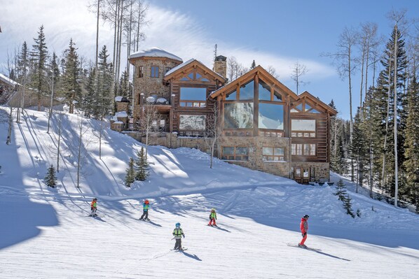 Une grande cabane en rondins, dotée de nombreuses fenêtres, avec une piste de ski au premier plan.