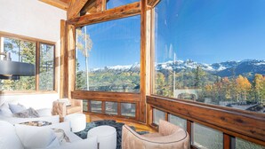 A spacious room with large windows offering a mountain view, a white sofa, a pink armchair, and a wooden ceiling. - PICTURE PERFECT- Stunning Ski-In/Out Trailside Manor Perfect for Groups (Mountain Village)