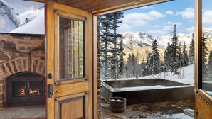 A wooden door leading to a stone fireplace, a hot tub, and a snowy mountain view. - PICTURE PERFECT- Stunning Ski-In/Out Trailside Manor Perfect for Groups (Mountain Village)