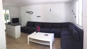Un salon moderne avec un canapé de couleur foncée, une table basse blanche ornée d’un vase et d’un livre, et une décoration murale représentant des poissons.