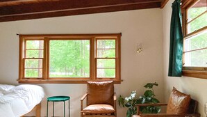 A room with a bed, two chairs, a table with glasses, and a window with curtains.