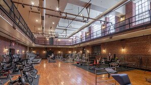 Ett rymligt gym med träningsutrustning, trägolv och väggar av tegel.