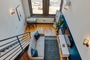 A modern interior with a staircase, a sofa, a small table, and a large window offering a view of the street.