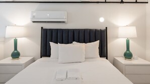 Un llit ben arrenjat amb llençols i almoades blanques, dues taules de nit amb làmpades i un aparell d'aire condicionat sobre el llit.