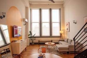 A modern living room with a sofa, a coffee table, a TV, and a staircase. - Sosuite | Studio Loft  Gym, Lounge (Philadelphia)