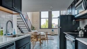A modern kitchen with a dining area, large windows, and a staircase. - Sosuite | Studio Loft w W/D, Gym, Lounge (Philadelphia)