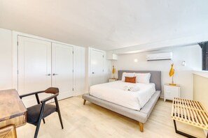 Een slaapkamer met een bed, nachtkastjes, een bureau en een stoel. Er staan witte kasten en een airconditioner aan de muur.