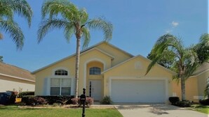 A two-story house with a garage, surrounded by well-maintained lawns and palm trees. - Beautiful Golf View Southern Dunes 4 Bedroom Villa by RedAwning (Haines City)