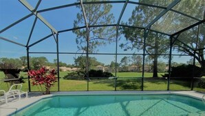 A clear swimming pool with a covered area, surrounded by a metal frame and glass panels, with a view of a grassy area and trees in the background. - Beautiful Golf View Southern Dunes 4 Bedroom Villa by RedAwning (Haines City)