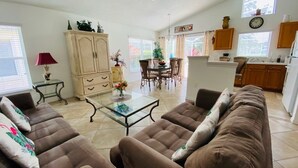 A living room with brown sofas, a glass coffee table, and a dining area with chairs and a table.