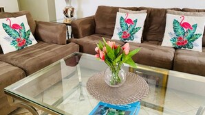 A living room with a brown sofa set, a glass coffee table with a vase of flowers, and a red lamp on a side table.