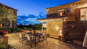 Edificio de piedra con patio que cuenta con una mesa y sillas, rodeado de plantas en macetas y un muro de piedra.