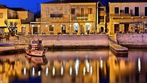 Un edificio frente al agua con fachada de piedra, un barco amarrado en primera línea y su reflejo en el agua.