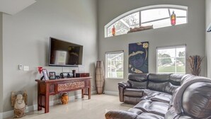 A spacious living room with a large leather sofa, a flat-screen TV, a wooden console table, and a large window with a view of the outdoors.