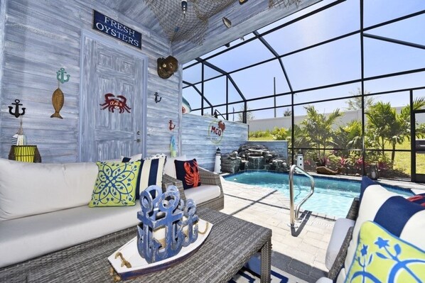 Un espace aménagé au bord de la piscine, avec un canapé blanc, des coussins décoratifs et une table agrémentée d’un centre de table.
