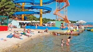 Una playa con parque acuático, que incluye un tobogán de agua grande y azul, y una estructura alta de color naranja.
