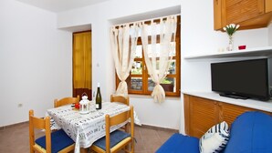 Una habitación pequeña y acogedora con una mesa de comedor, sillas, un sofá, un televisor y una ventana con cortinas.