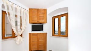Ein kleines Zimmer mit einem Bett, einem Fernseher, Holzschränken und zwei Fenstern.