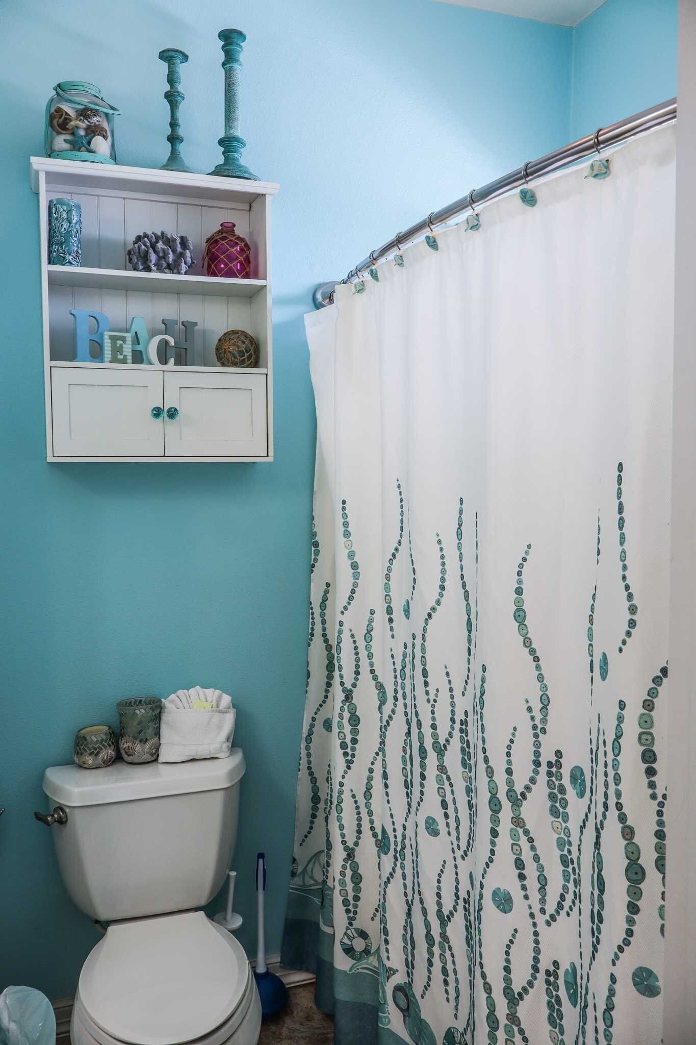 Un baño con inodoro, repisa con adornos y cortina de ducha estampada con hojas.