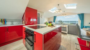 Une cuisine moderne avec des meubles de couleur rouge, un îlot central et une vue sur la mer grâce à de grandes fenêtres.