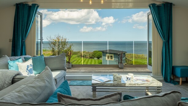 Un salon spacieux doté d’une grande fenêtre donnant sur la mer et sur un petit bâtiment.