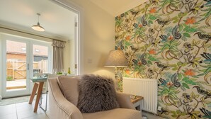 A living room with a beige armchair, a table, and a patterned wallpaper. - Acorn Cottage (H), Holt, Norfolk (Holt)