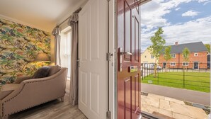 A room with a beige sofa, a patterned wall, and a view of a brick house through a glass door. - Acorn Cottage (H), Holt, Norfolk (Holt)