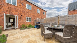 A patio with a brick house, a wooden fence, and a table with chairs. - Acorn Cottage (H), Holt, Norfolk (Holt)