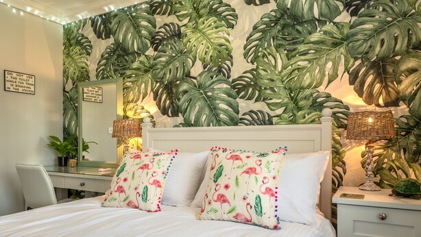 A bedroom with a large bed, two bedside tables with lamps, a desk, and a chair. The walls are decorated with a tropical leaf pattern. - Acorn Cottage (H), Holt, Norfolk (Holt)