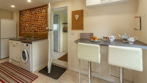 Cocina compacta con lavadora, pared de ladrillo, un tablón de corcho con forma de corazón y una pequeña zona de bar con taburetes.