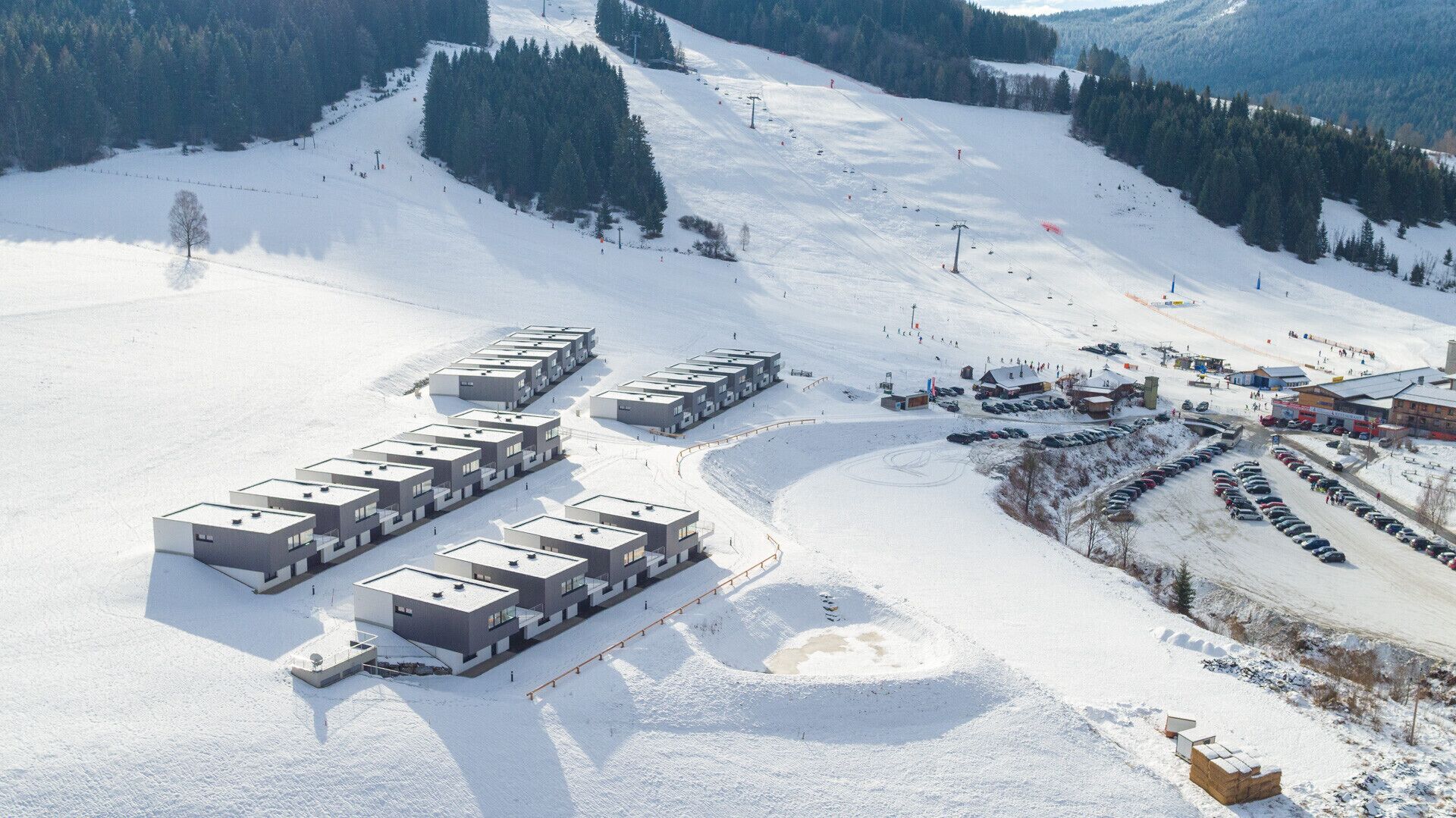 Ein modernes Skigebiet mit mehreren Gebäuden, Skipisten und einem Parkplatz.