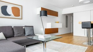 Un salon moderne avec une table basse en verre, un canapé gris et un lampadaire noir.