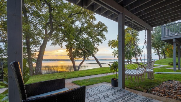 A covered outdoor seating area with wicker furniture and a patterned rug, overlooking a lake and trees. - Spacious 4 bedroom on Lake Le Home Dieu (Alexandria)