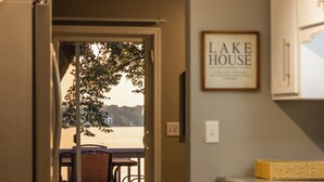A view from a room with a door leading to a balcony overlooking a body of water, a framed sign on the wall, and a kitchen area with cabinets and a countertop. - Spacious 4 bedroom on Lake Le Home Dieu (Alexandria)