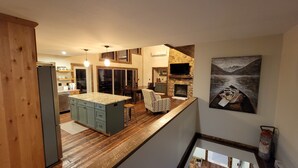 A spacious kitchen with a large island, wooden flooring, and a stone fireplace.
