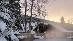 Ein Whirlpool, umgeben von schneebedeckten Bäumen und einem Holzzaun.