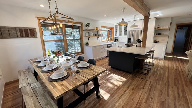 Eine moderne Küche mit Holzboden, einer zentralen Kochinsel und einem Essbereich mit einem für sechs Personen gedeckten Holztisch.