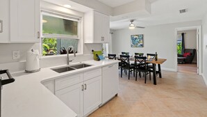 Una cocina moderna con armarios blancos, un ventanal grande y un comedor con mesa y sillas de madera.
